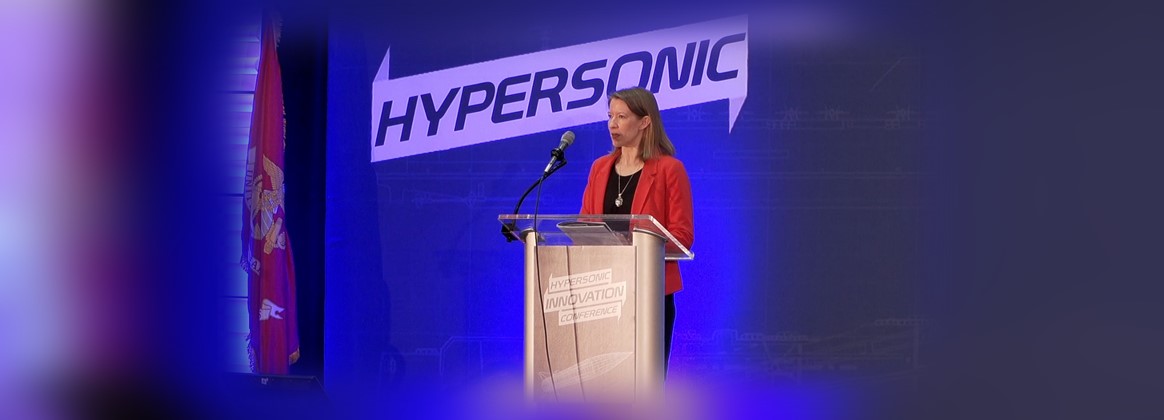 A woman stands in front of a podium, speaking at a conference.